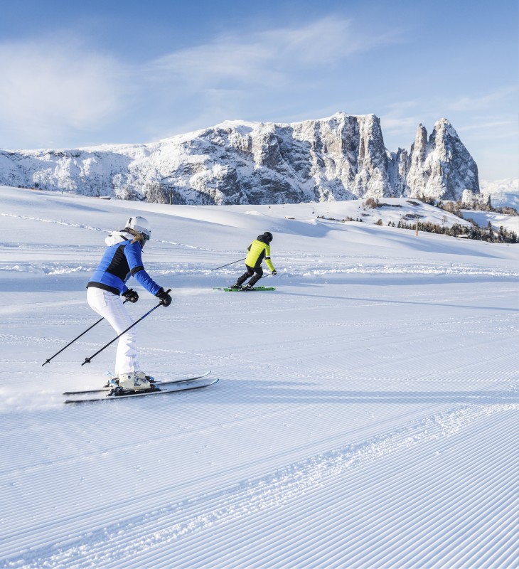 The Seiser Alm ski area. In the foreground are two skiers skiing down the piste and in the background you can see the Schlern.