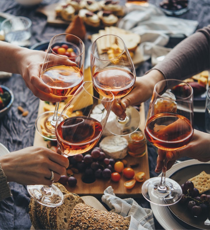 Ein Esstisch mit einer Marende und Brotkörben. Darüber stoßen die Gäste mit ihrem Aperitif an.