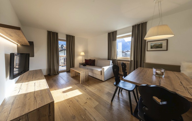 Der Wohnbereich des Appartements. Man sieht den TV und die Couch sowie den Esstisch mit schwarzen Stühlen.