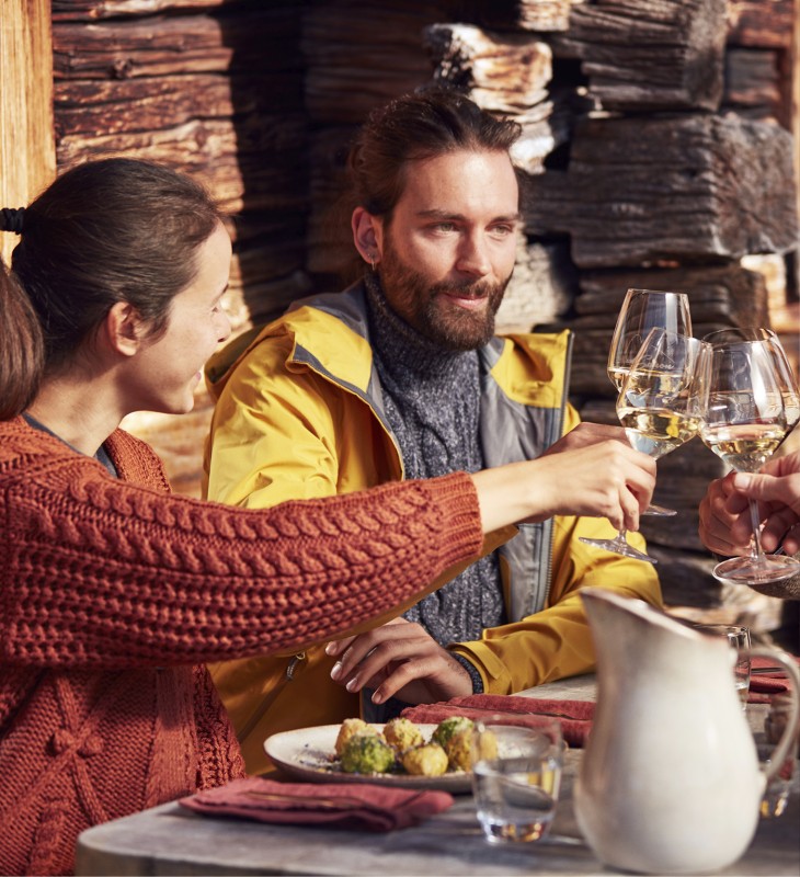 Ein Paar auf einer Almhütte isst geradezu  Mittag und trinkt ein Glas Südtiroler Weißwein.