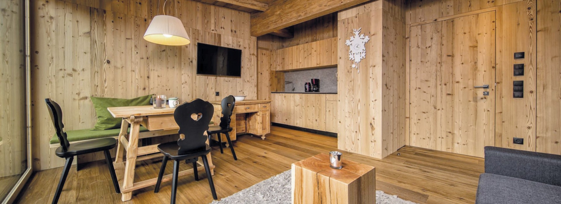 Der Wohnbereich einer Ferienwohnung, in dem du einen Holztisch mit schwarzen Stühlen und die Küche im Hintergrund vorfindest.