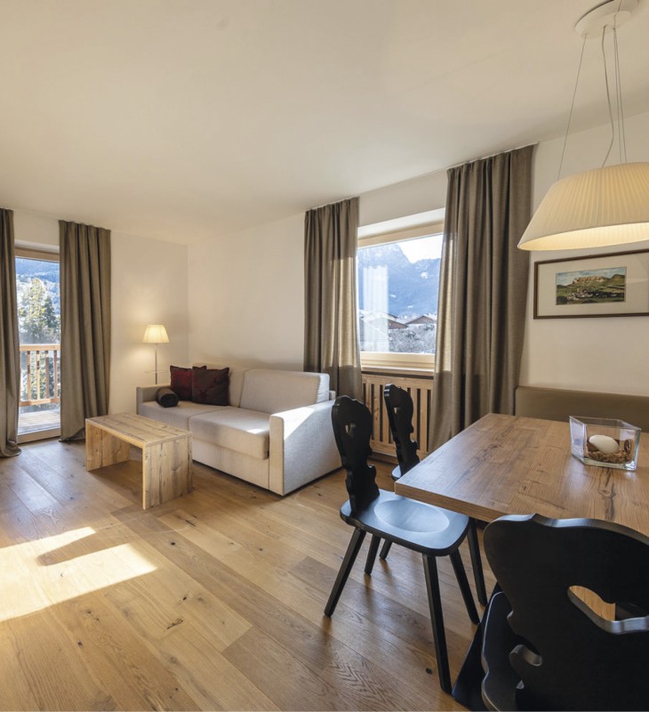 Das Bild zeigt den Wohnbereich der Wohnung. Man sieht eine Couch und den Esstisch sowie den Balkon.