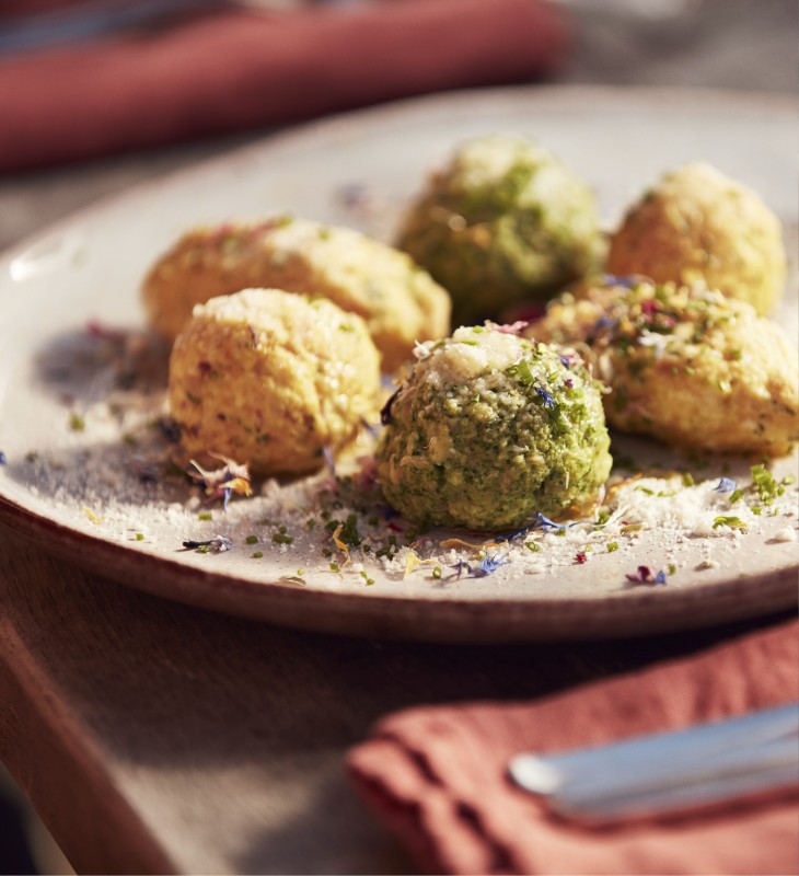 Ein Teller mit frei verschiedene Knödelsorten, die mit brauner Butter und Parmesan bestreut sind.