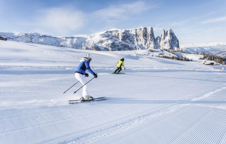Das Skigebiet Seiser Alm und zwei Skifahrer sowie den Schlern im Hintergrund.