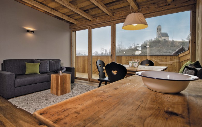 Wohnbereich des Zimmers. Man sieht eine Couch, einen Holztisch mit schwarzen Stühlen und den Balkon mit Aussicht.