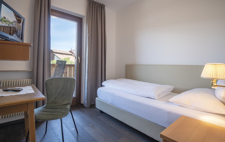 Einzelzimmer mit Bett, Schreibtisch und TV. Es ist auch ein Teil des dazugehörigen Balkons zu sehen.