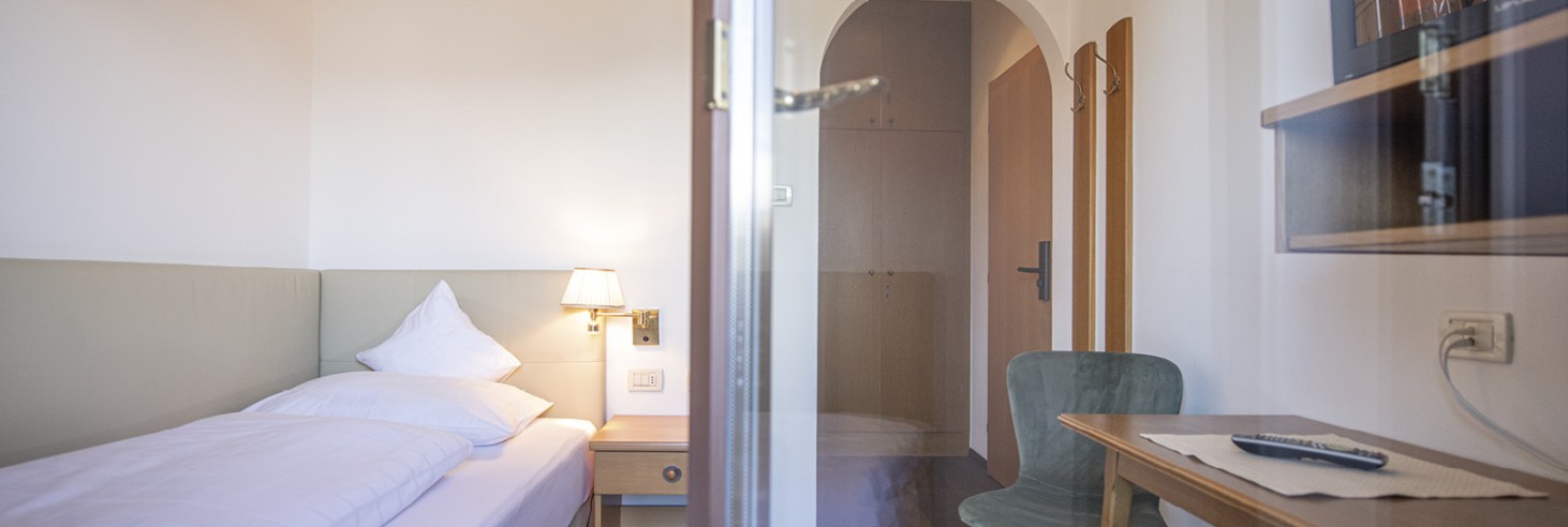 Un letto singolo con scrivania e televisore. La foto è stata scattata dal balcone.