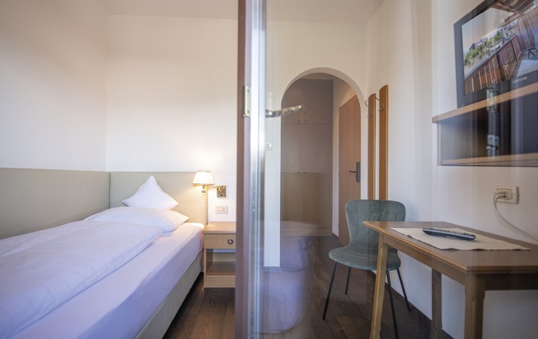 Einzelbett mit Schreibtisch und Fernseher. Das Bild wurde vom Balkon aus gemacht.